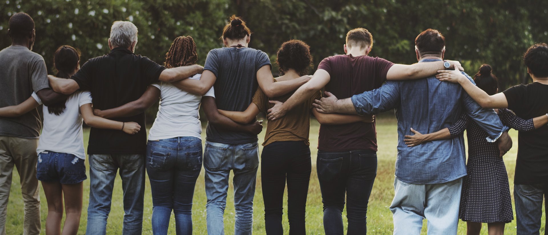 Das Foto zeigt eine Gruppe Menschen von hinten, die sich gemeinschaftlich umarmen